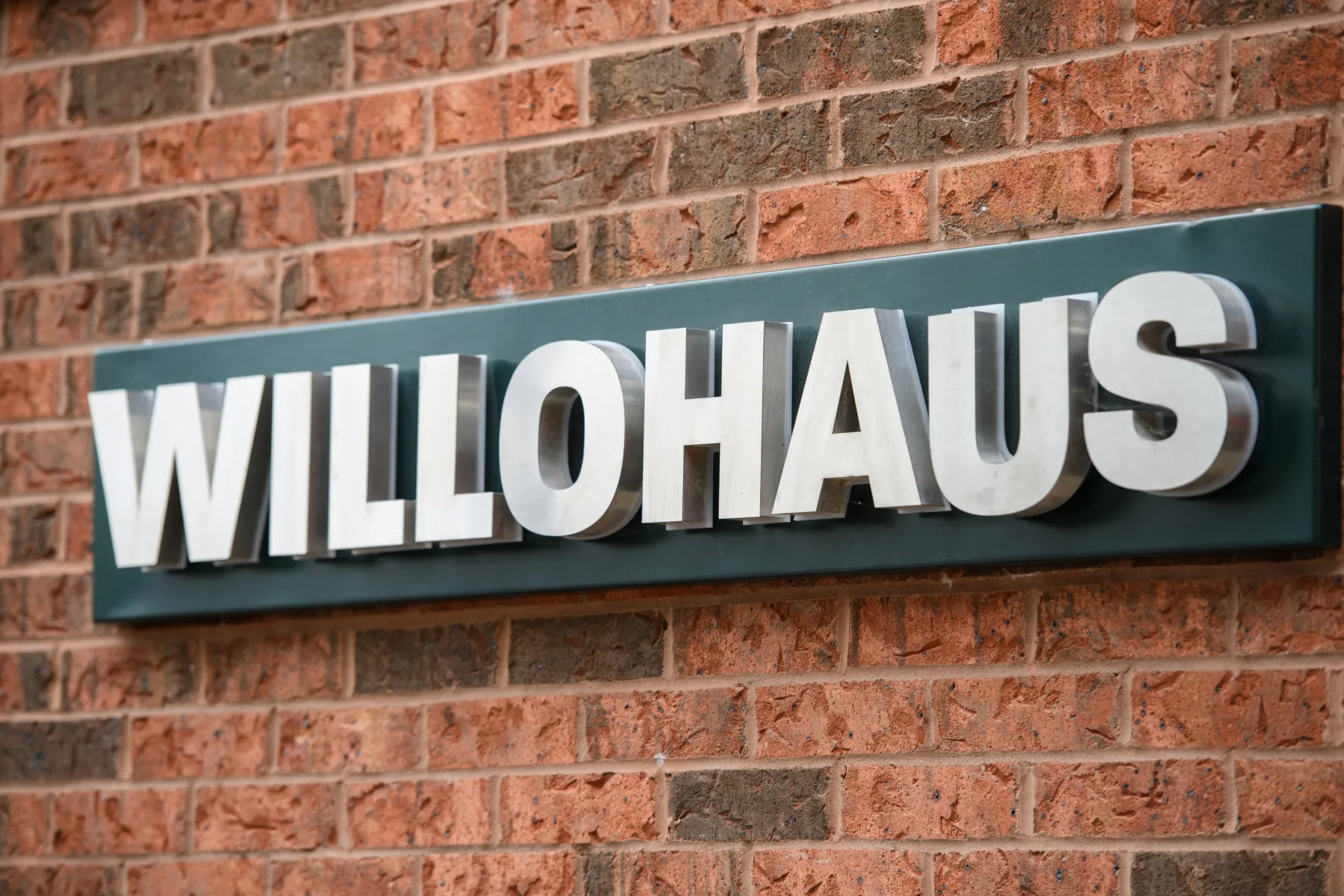 Willohaus building sign in brushed metal lettering fixed to a red-brick wall.