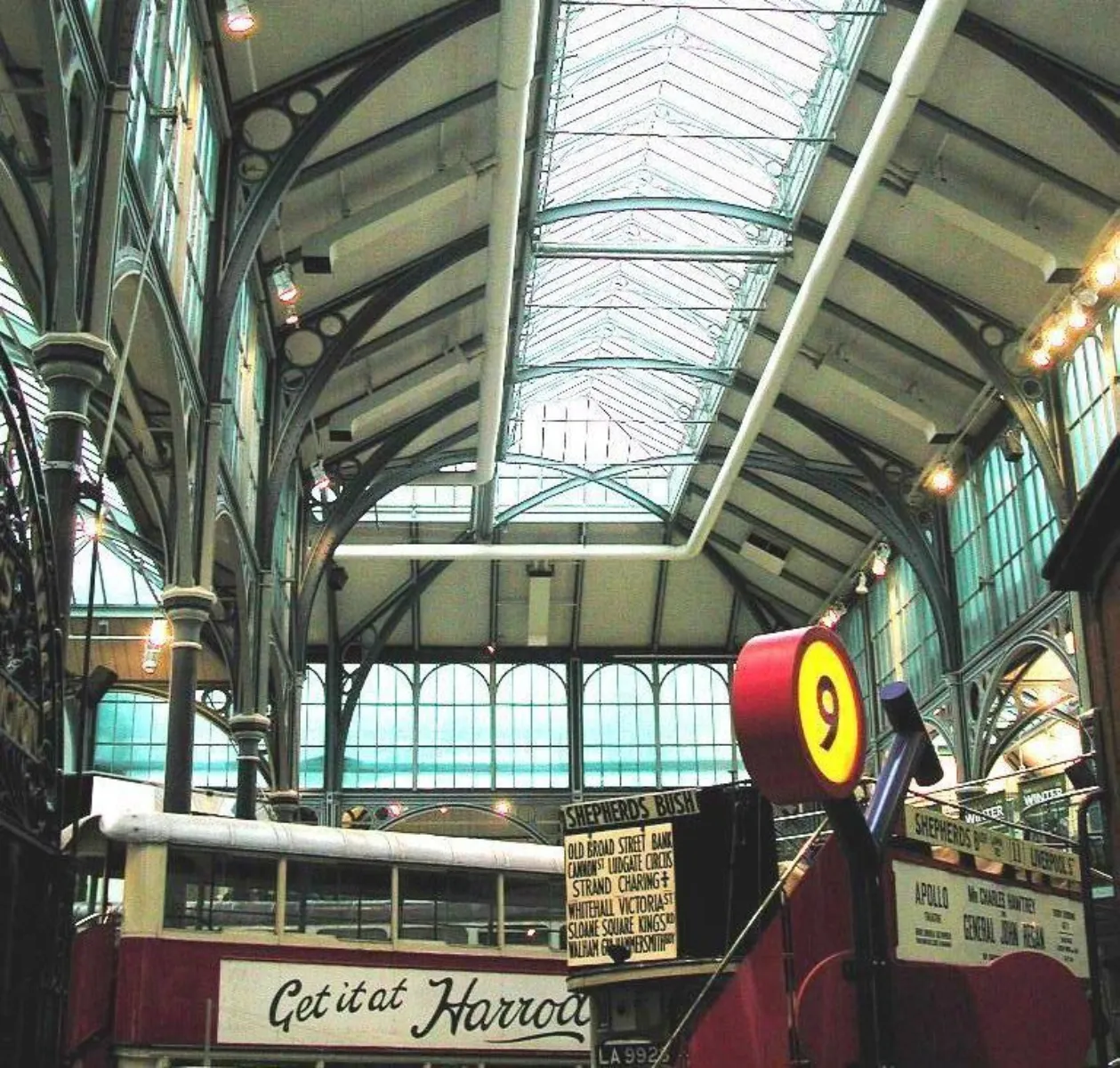 nterior of a Victorian-style transport museum with a vaulted glass roof, cast-iron columns, hanging destination signs, and vintage transport displays below.