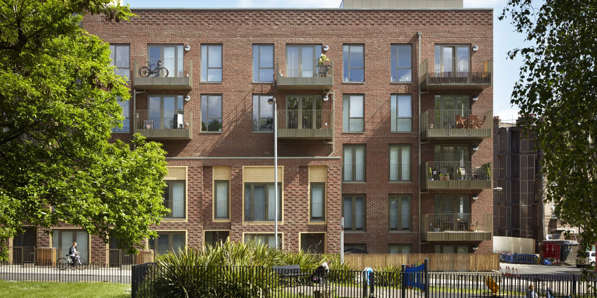 The exterior of a new build brick block of flats with a central planted courtyard on a sunny day