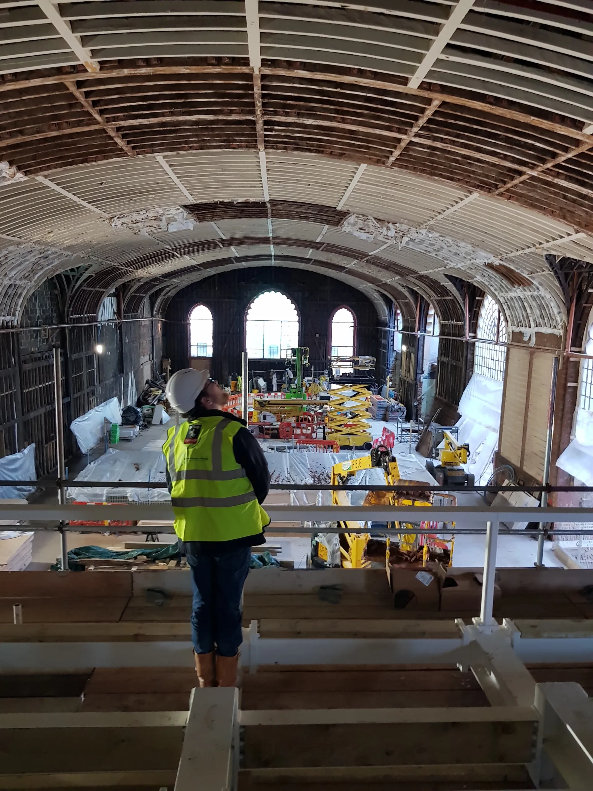 An engineer in a hard hat and high-vis vest looks up towards the ceiling of brighten dome