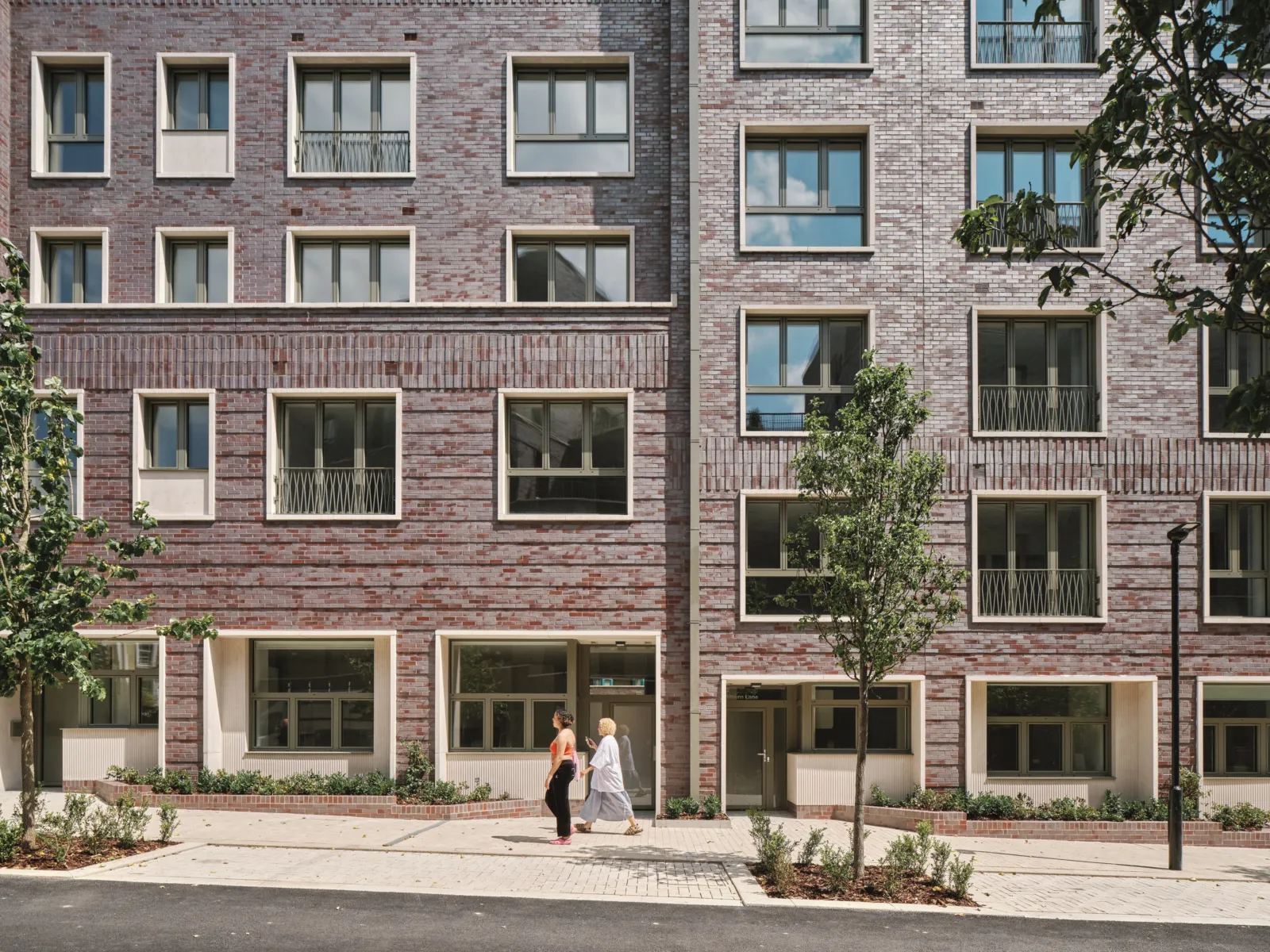 two people walking up a gently sloped sidewalk in front of a brick building