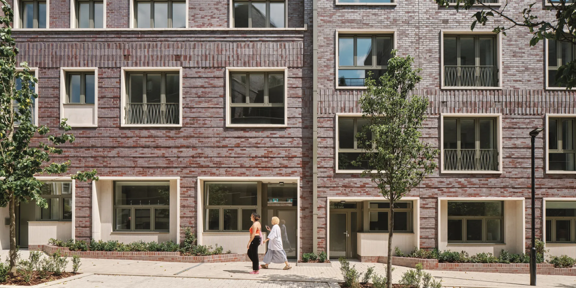 two people walking up a gently sloped sidewalk in front of a brick building