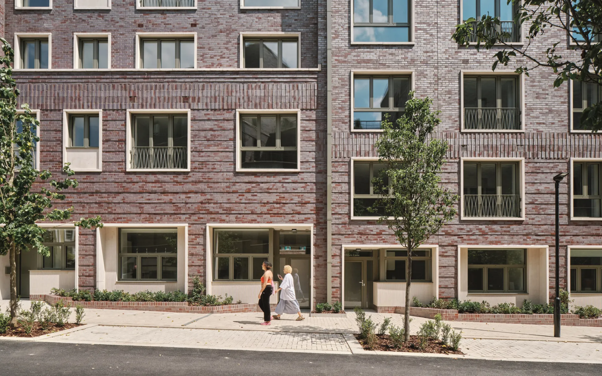two people walking up a gently sloped sidewalk in front of a brick building