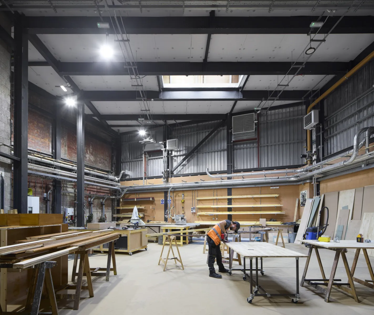A high-ceilinged workshop in a theatre showing tools, wood, tables and someone working