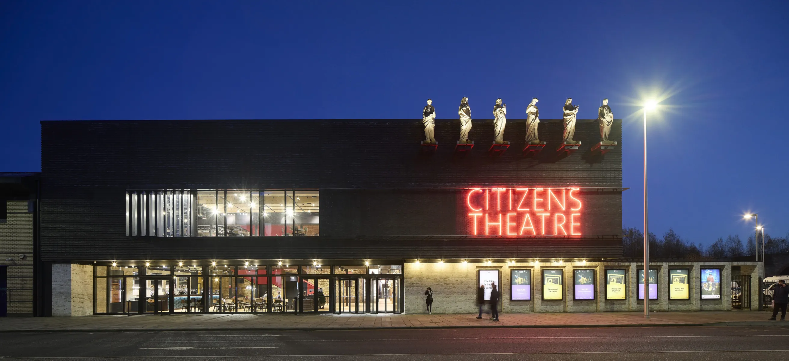 nighttime image showing the external facade of a building with statues mounted near the roof