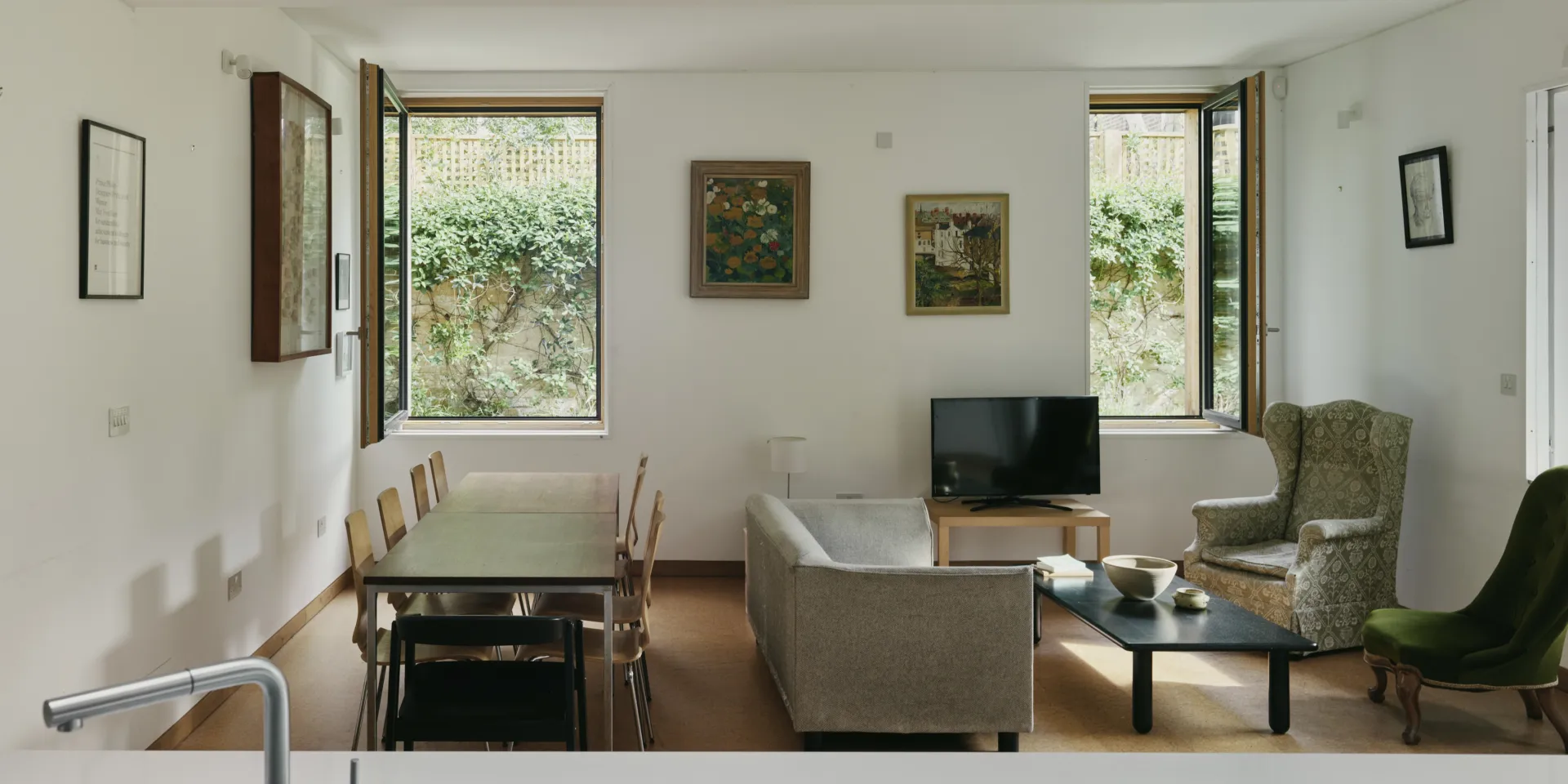 A living room with dining room, sitting chairs and two windows open to the gardens.
