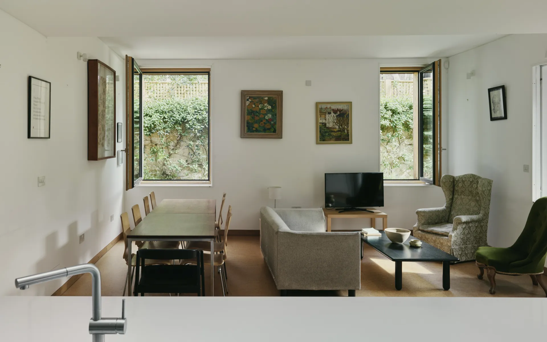 A living room with dining room, sitting chairs and two windows open to the gardens.