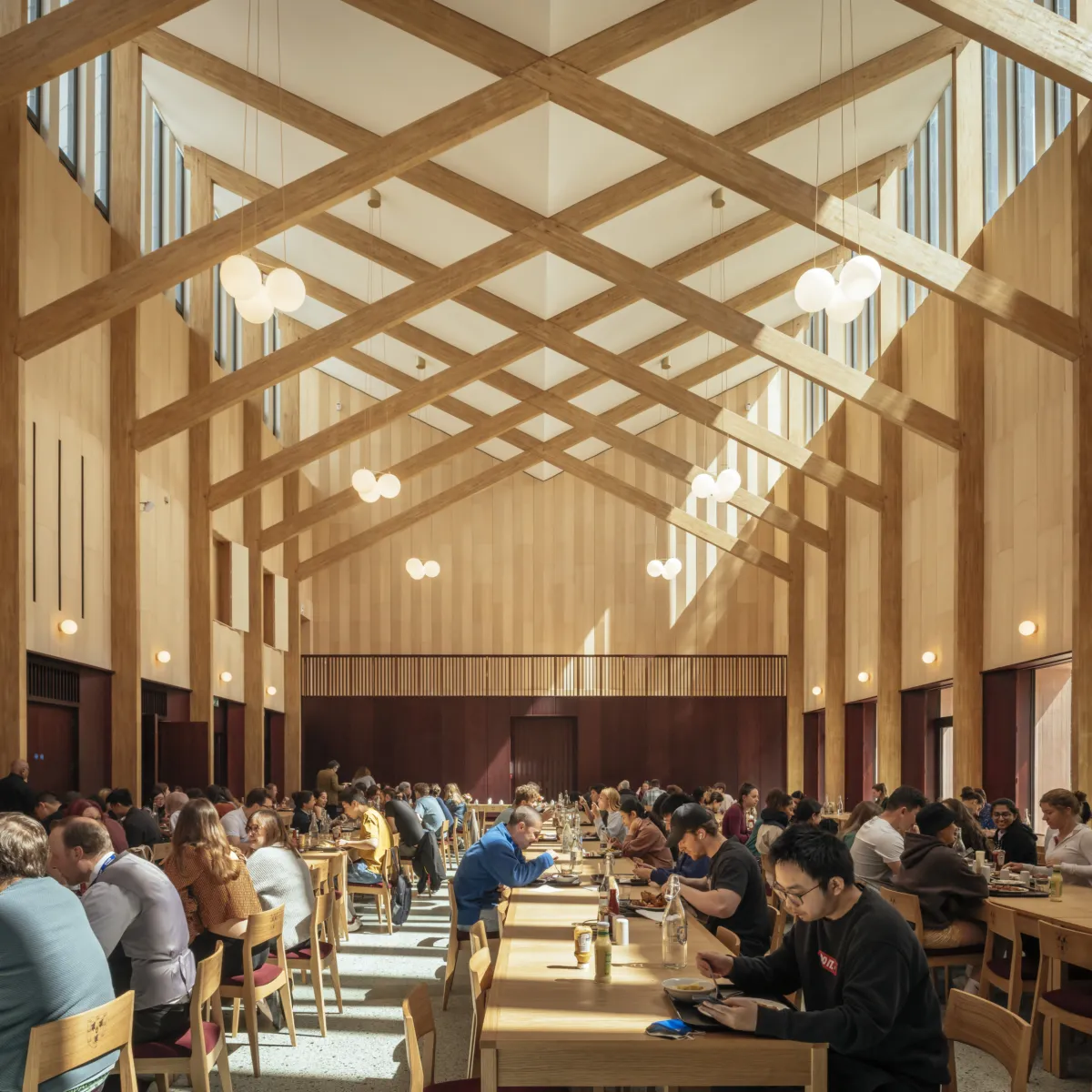 Day-lit dining hall with wooden beams and students eating