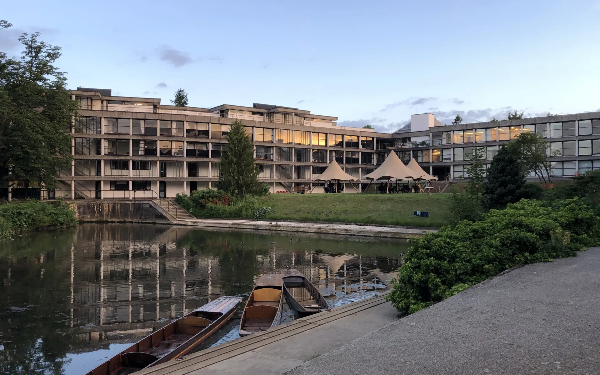Image show a modernist building with a small lake in front