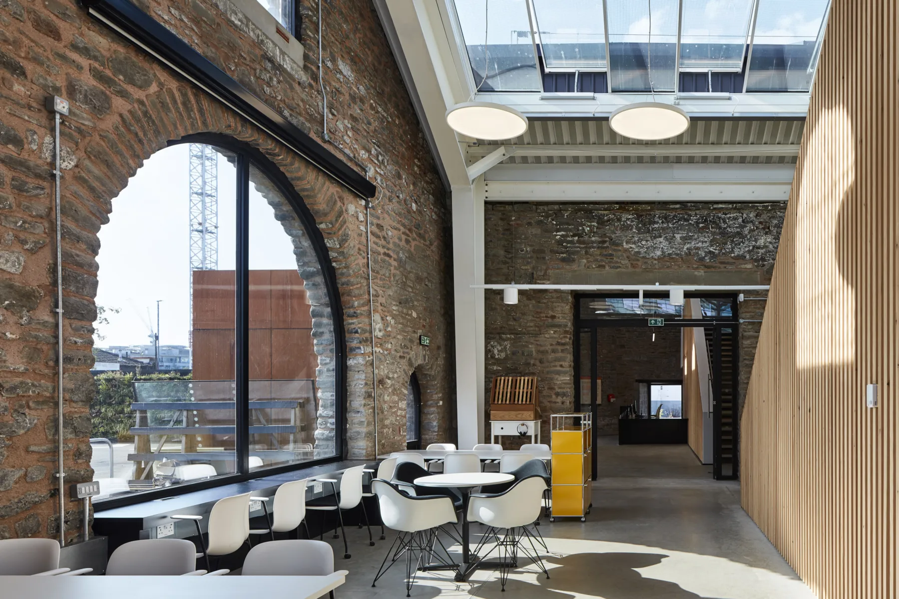 Image shows large window within brick wall, skylights and tables and chairs.