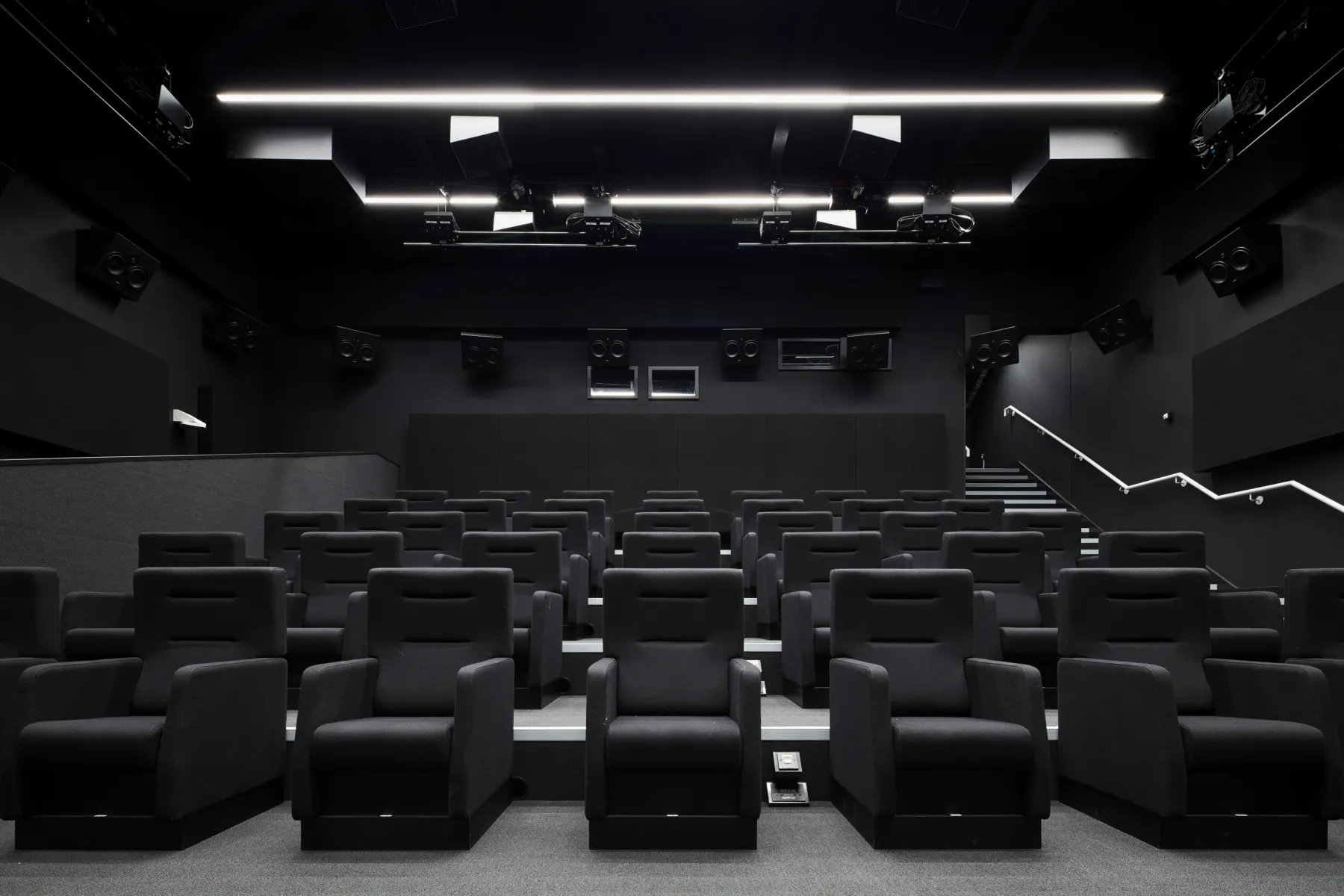 Image shows a dark theatre with black chairs