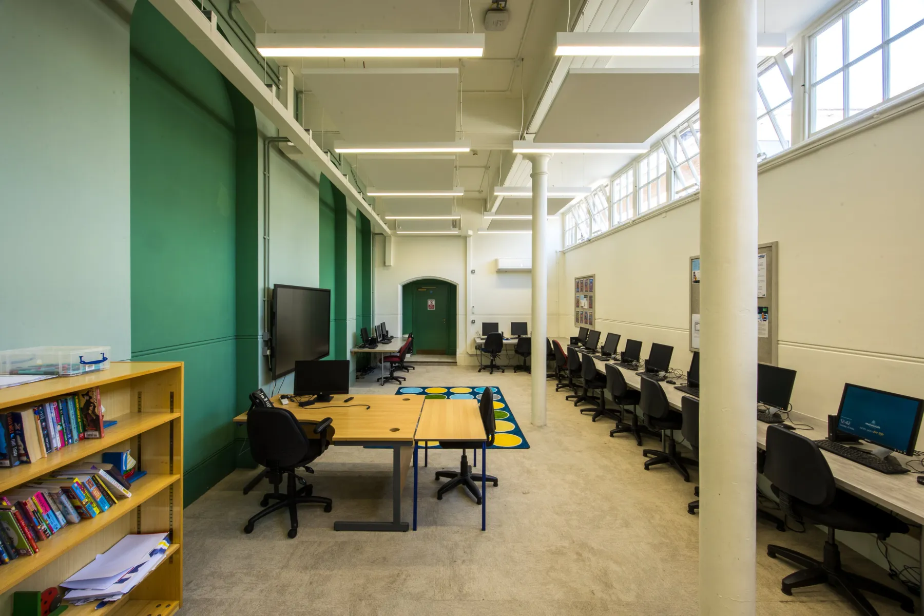 Computer room with desks, monitors, and shelving along a high-ceilinged space.