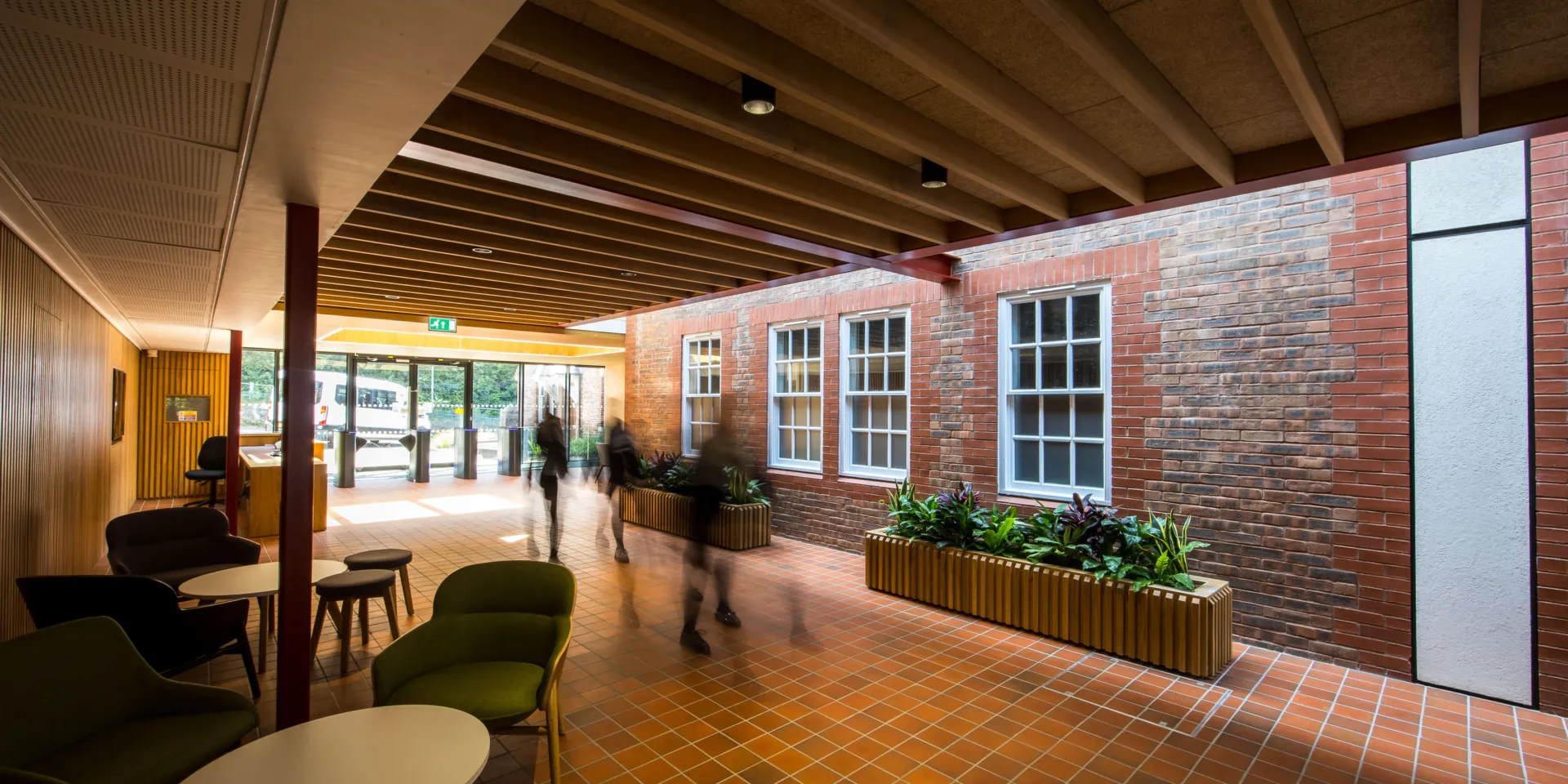 Entrance lobby with brick wall, planters, seating, and people moving through the space.