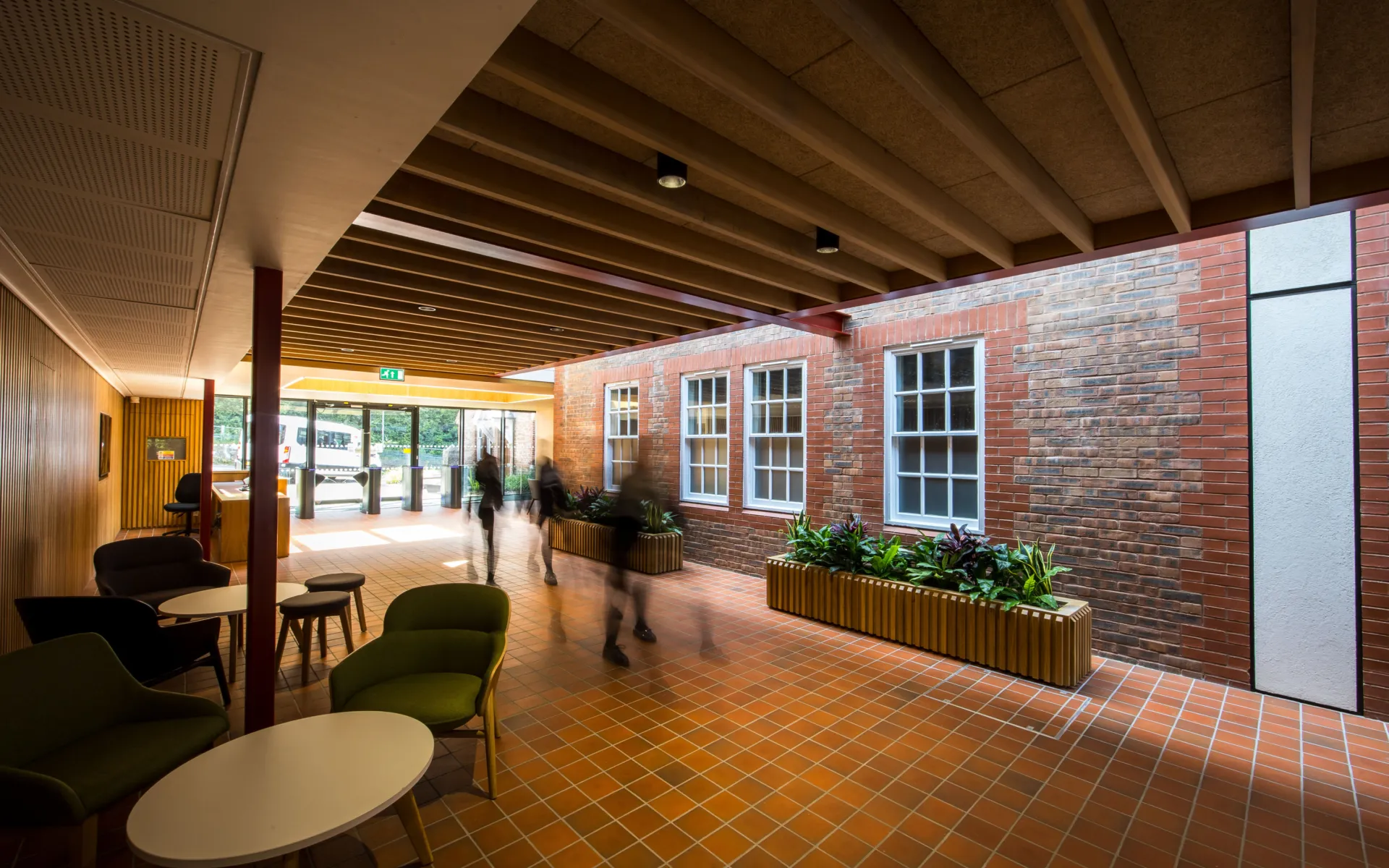Entrance lobby with brick wall, planters, seating, and people moving through the space.