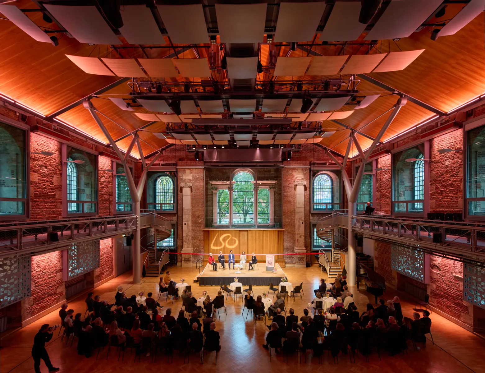 Wide view of auditorium with panel discussion on stage and audience seated below.