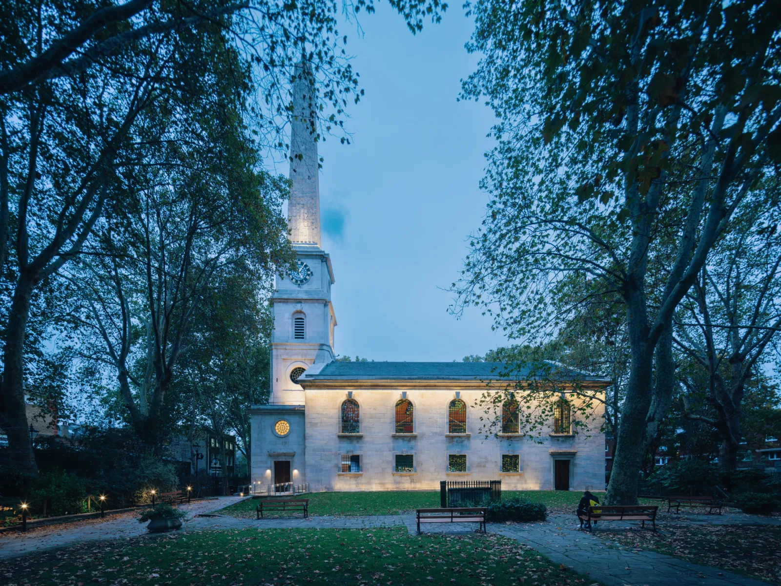 Exterior of historic church-like building at dusk surrounded by trees and benches.