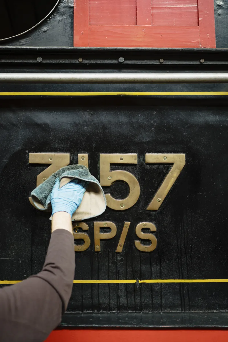 person cleaning the printing on the side of a steam locomotive engine