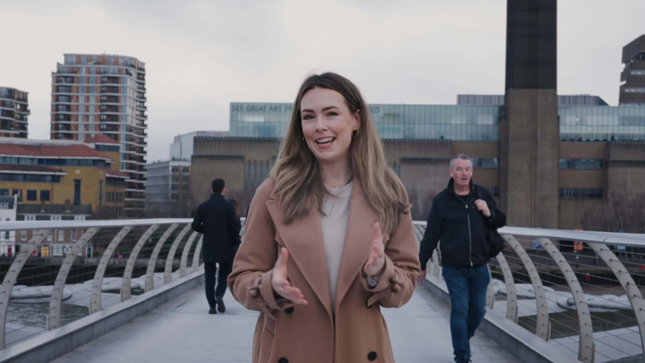 Imogen Bhogal speaking to the camera on Millenium Bridge in front of Tate Modern