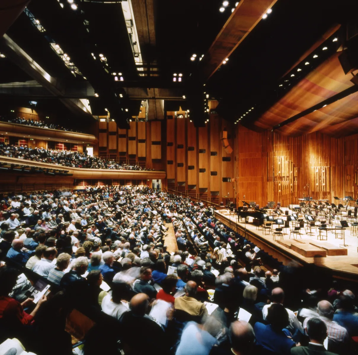 Wide view of a modern concert hall interior with tiered blue seating and a wooden stage set.