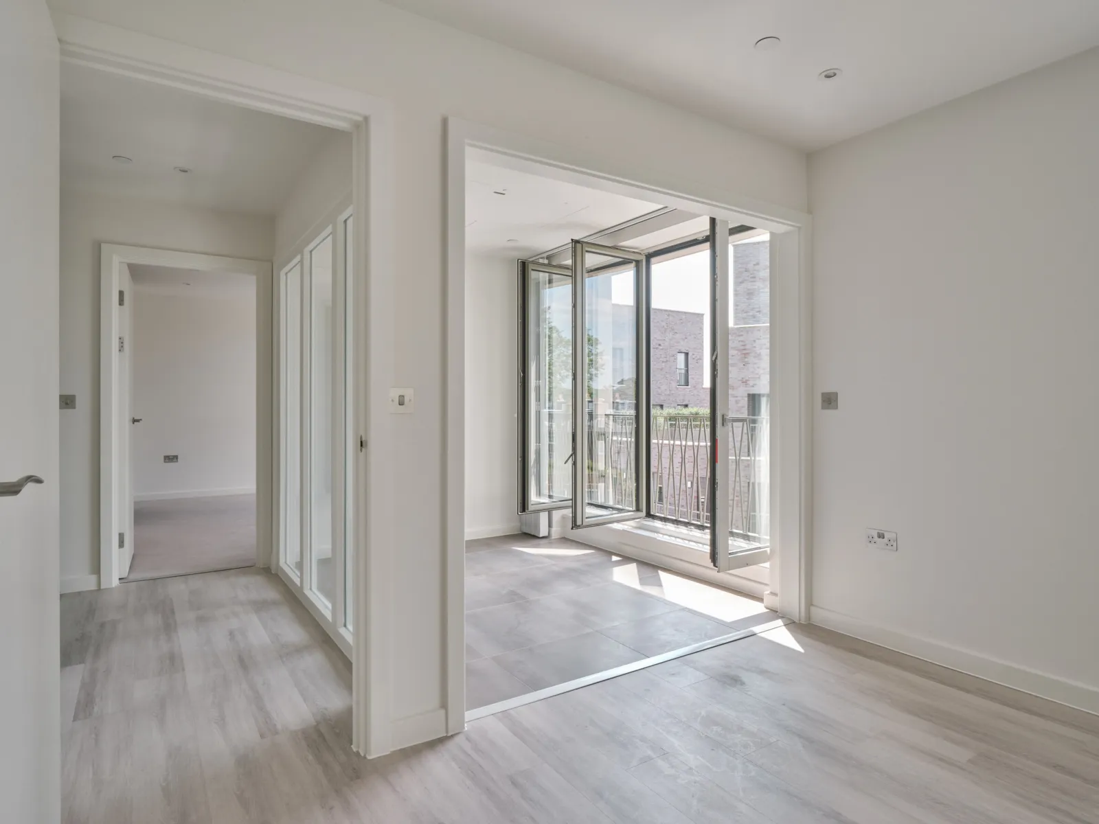 Bright, empty apartment interior with floor-to-ceiling glazed doors opening onto a balcony.