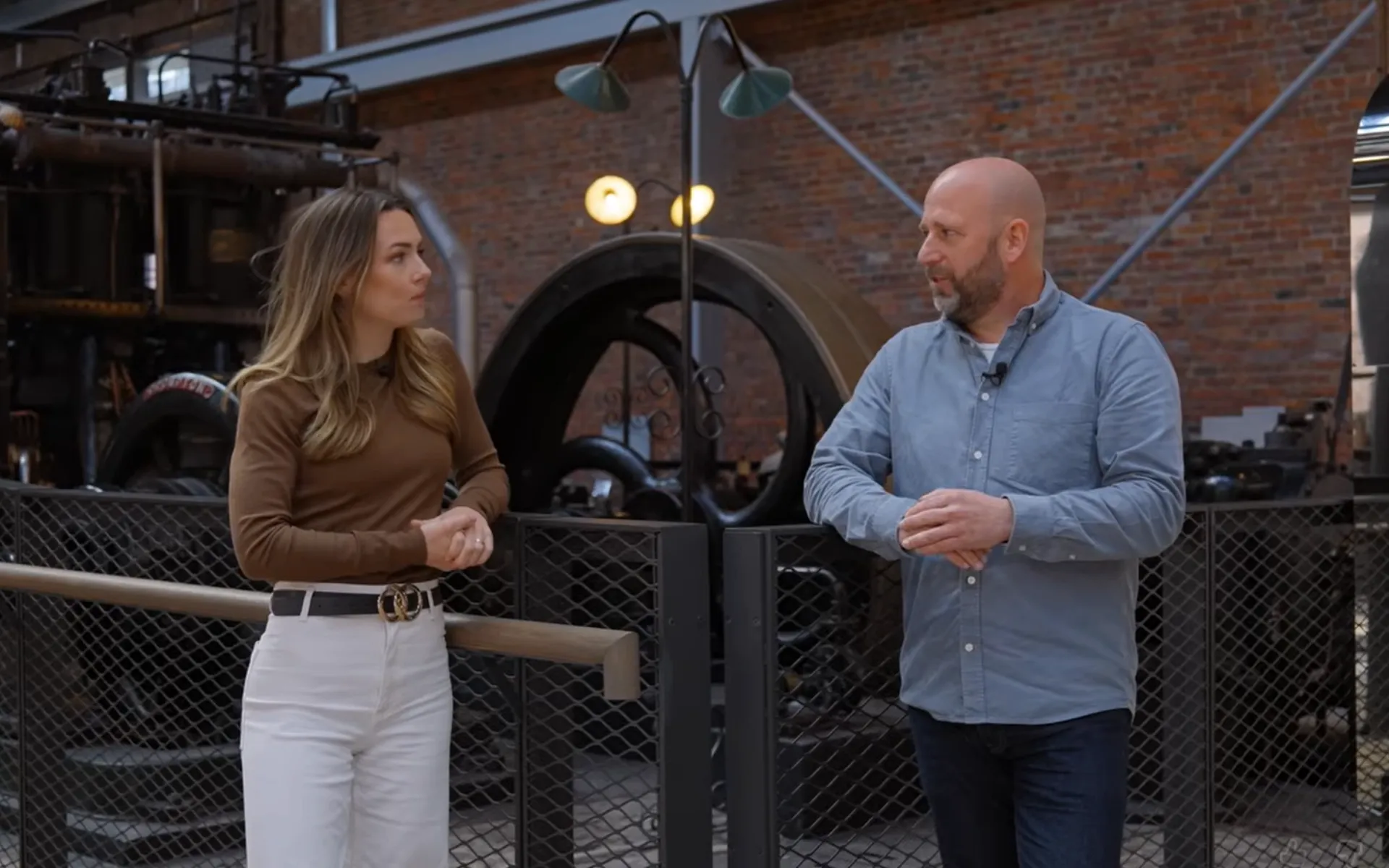 A man and a woman are stood on front of an old engine at a museum talking