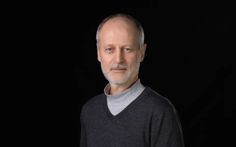 A headshot of Colin Darlington wearing a dark grey jumper over a high-neck grey top