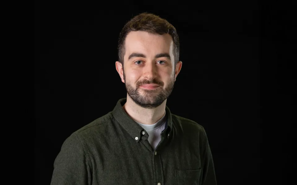 A headshot of Conor Haselden wearing a dark grey shirt over a white t-shirt