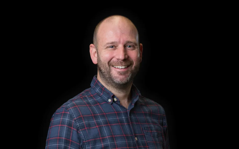 A headshot of Iain Shaw wearing a navy checkered shirt
