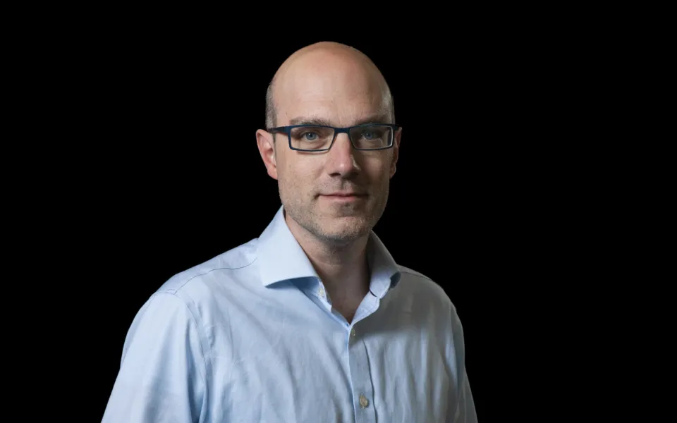 A headshot of Innes Johnston wearing glasses and a blue shirt