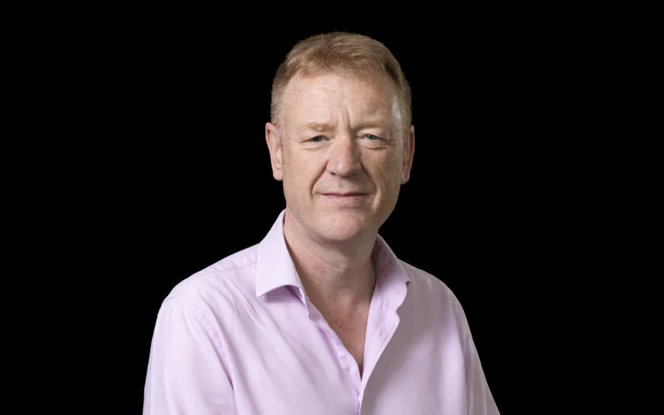 A headshot of Alasdair Reid wearing a pink shirt