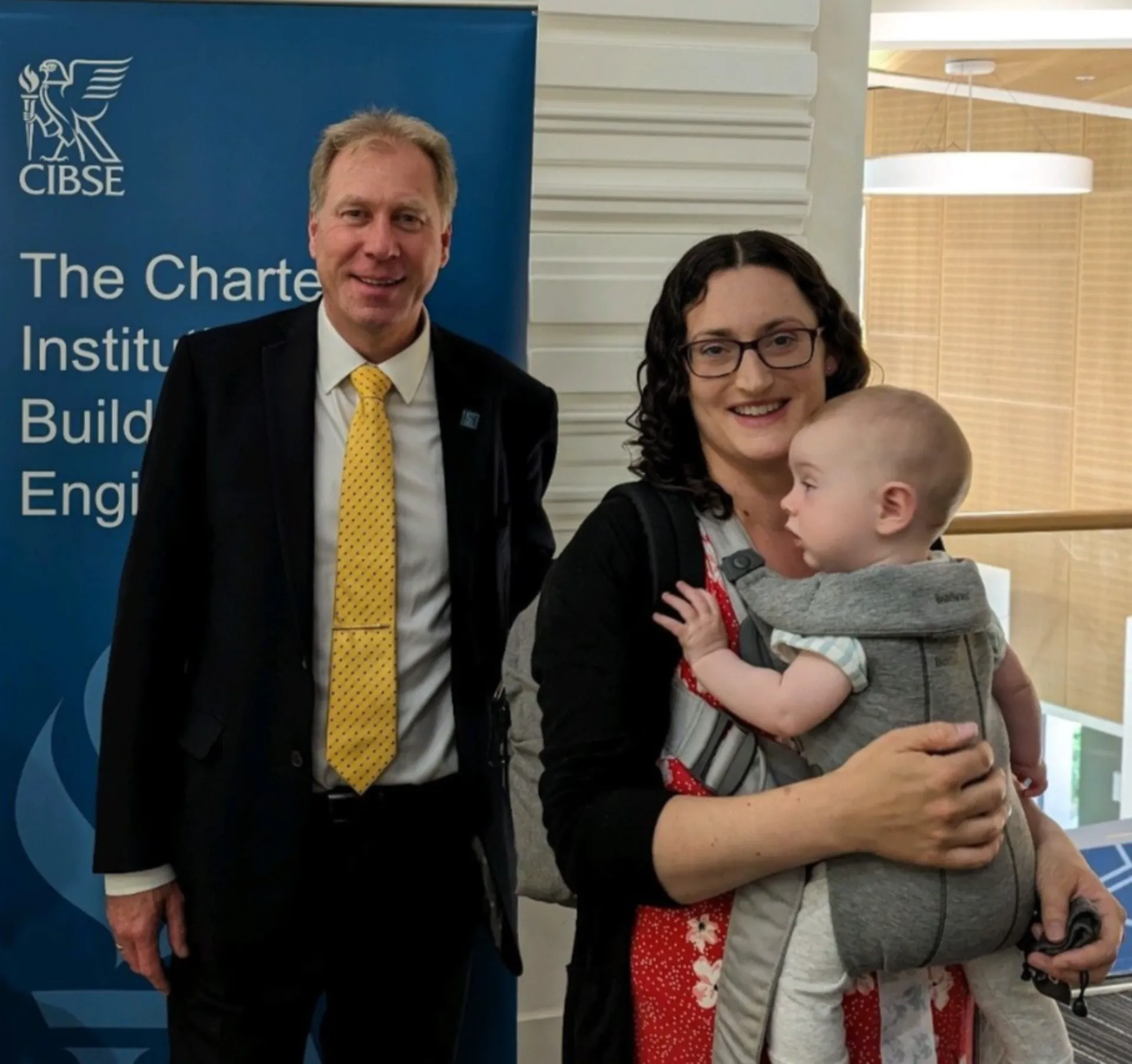 Man and woman who is holding a baby in front of a banner.