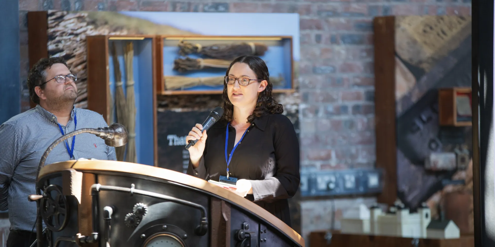 woman standing at a podium with man looking into the distance