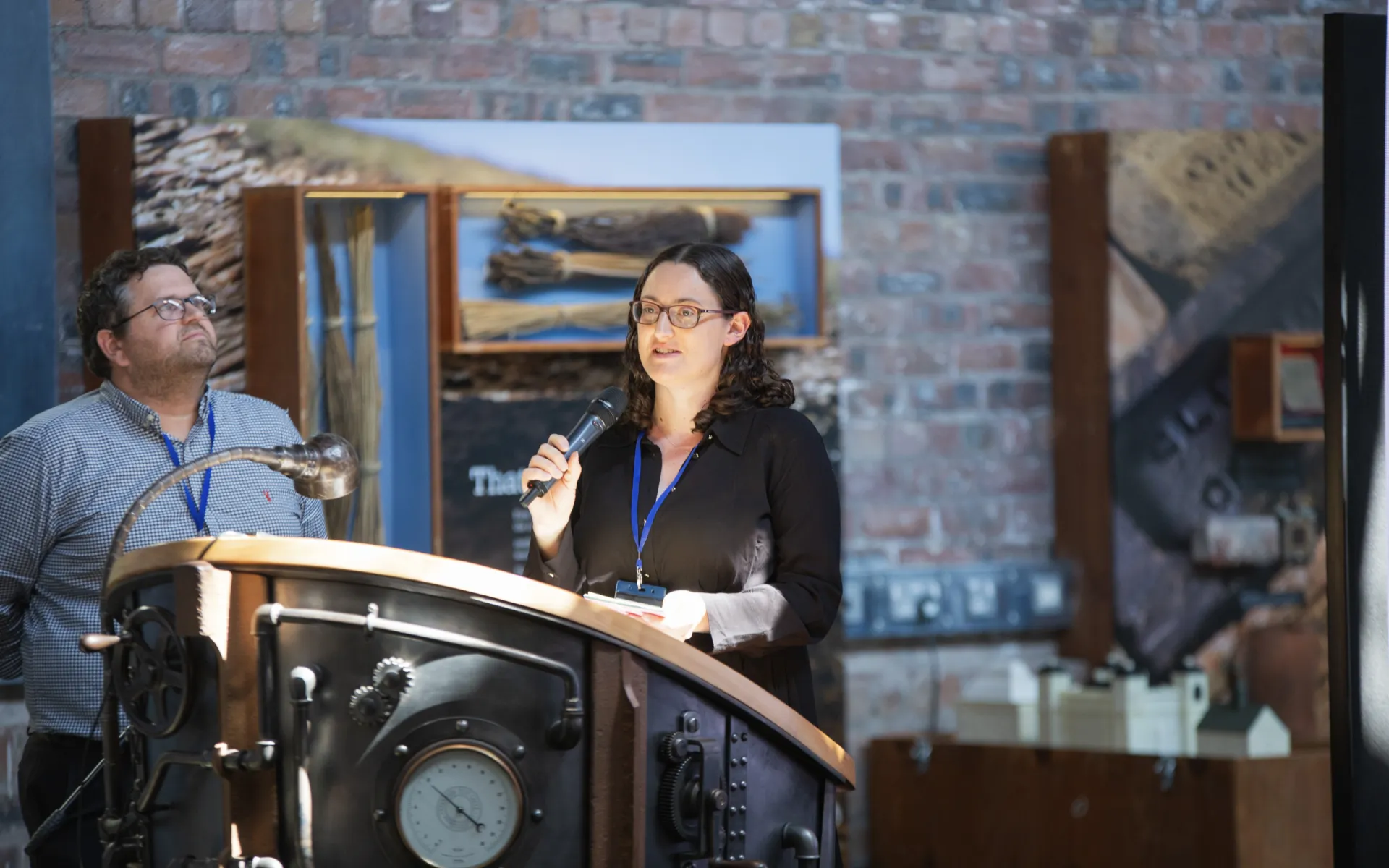 woman standing at a podium with man looking into the distance