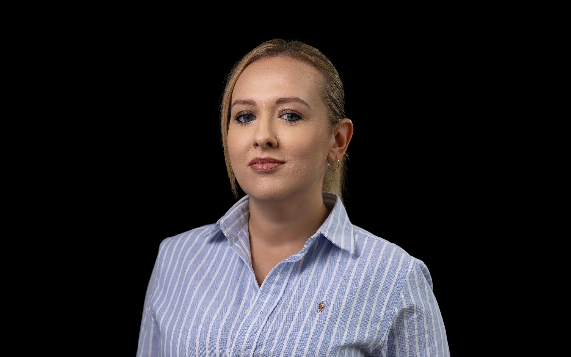 Head and shoulders portrait photo of Emma with her hair tied back, and wearing a blue and white striped shirt.