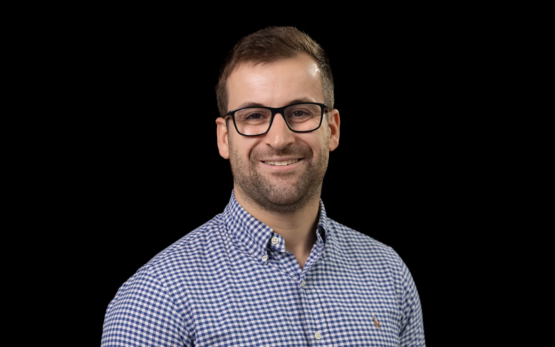 Head and shoulders portrait photo of Joe in glasses and a blue and white checked shirt.