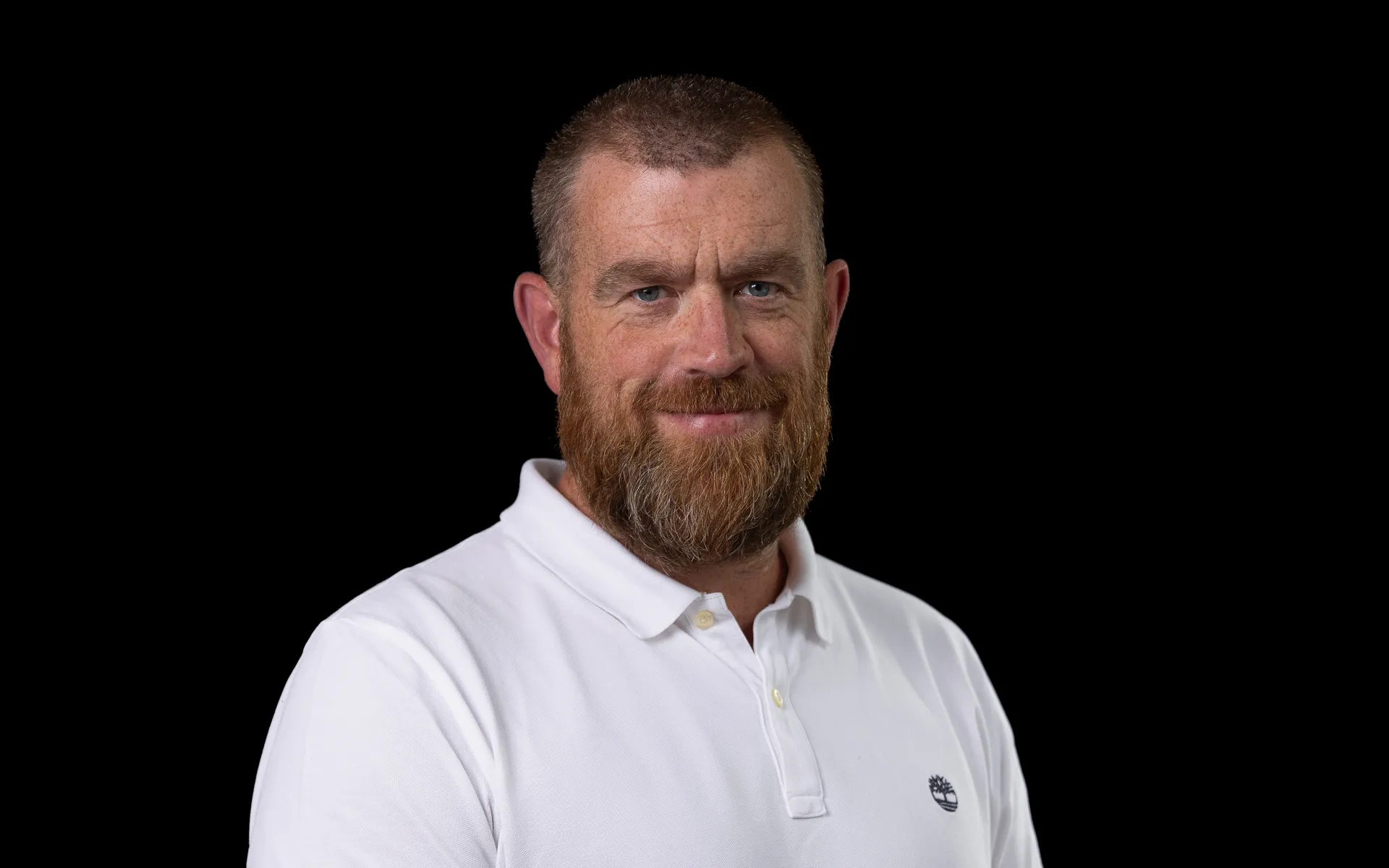 Close-up portrait photo of Niall smiling at the camera, wearing a white shirt and with a full beard.