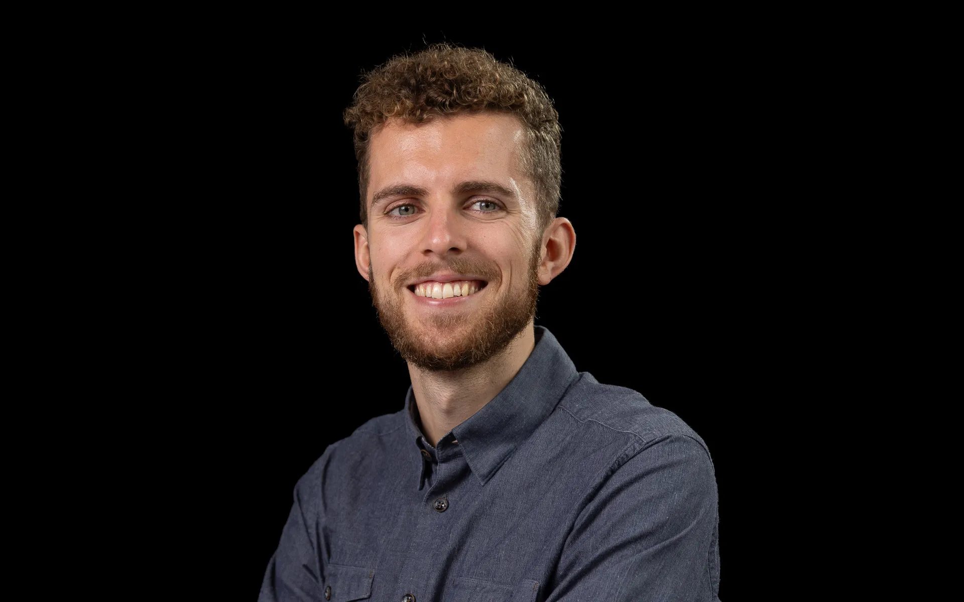 Photo of Tom in a grey-blue shirt, smiling at the camera