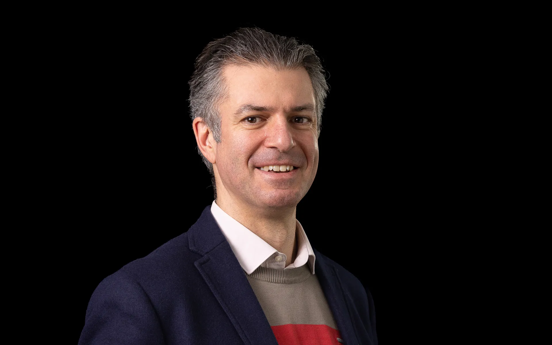 A headshot of Gwilym Still smiling at the camera, wearing a dark jacket and white shirt