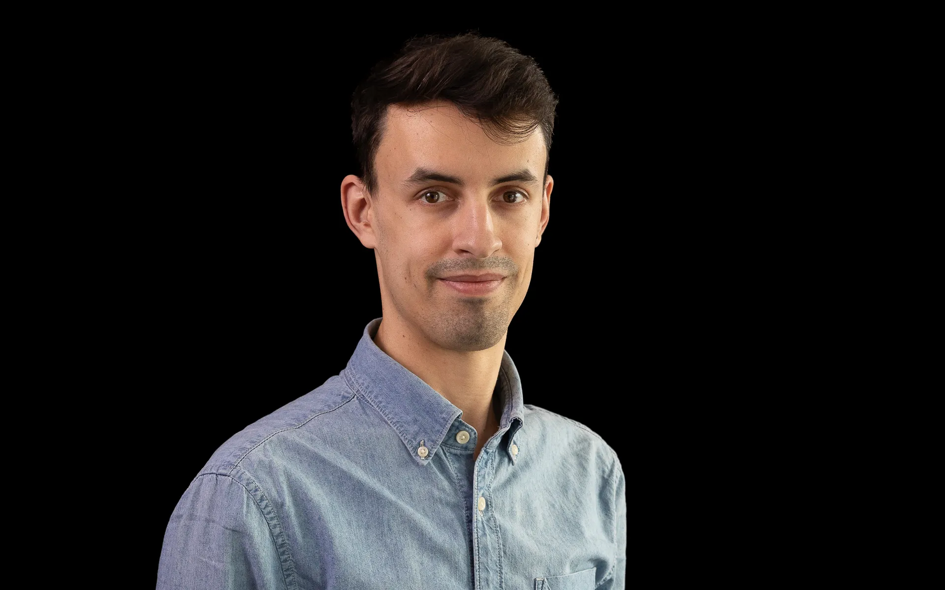 Studio portrait of a man wearing a light blue button-down shirt, photographed against a black background.