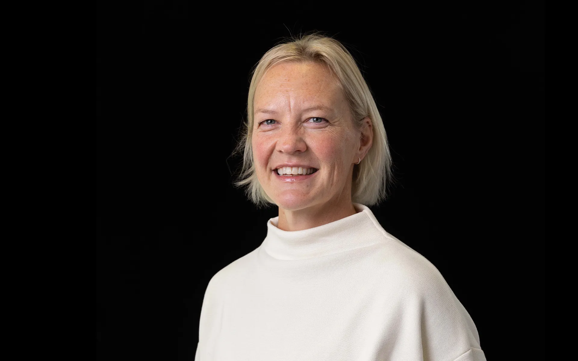 Photo of person with blonde hair, wearing a white high-necked top, against a black background.