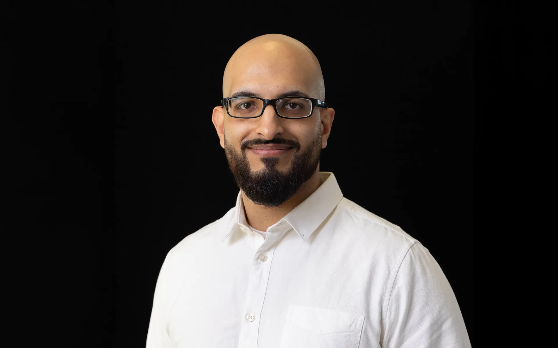 A portrait of Abubackar Ashraf wearing a white shirt against a black background.
