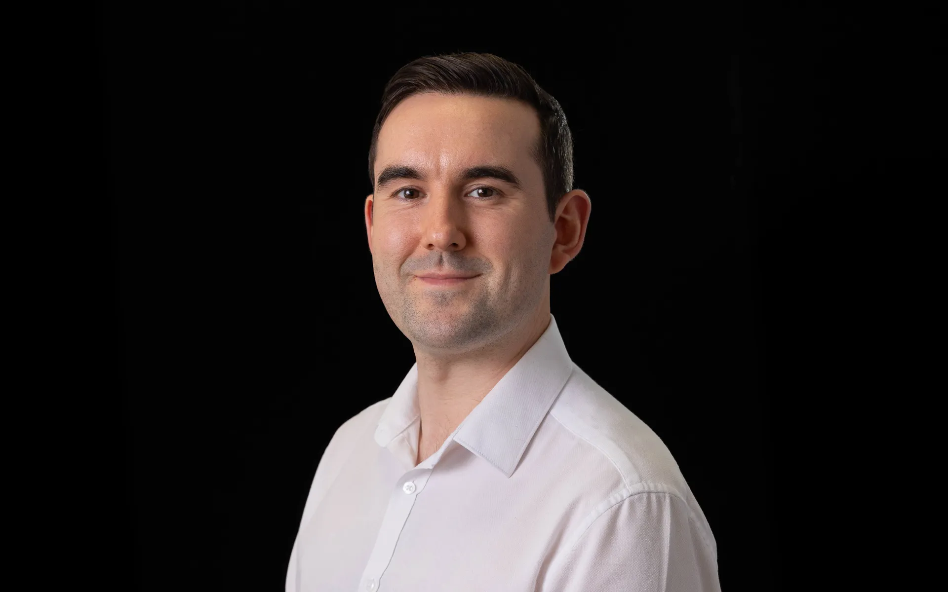 A portrait of Alec wearing a white shirt against a black background.