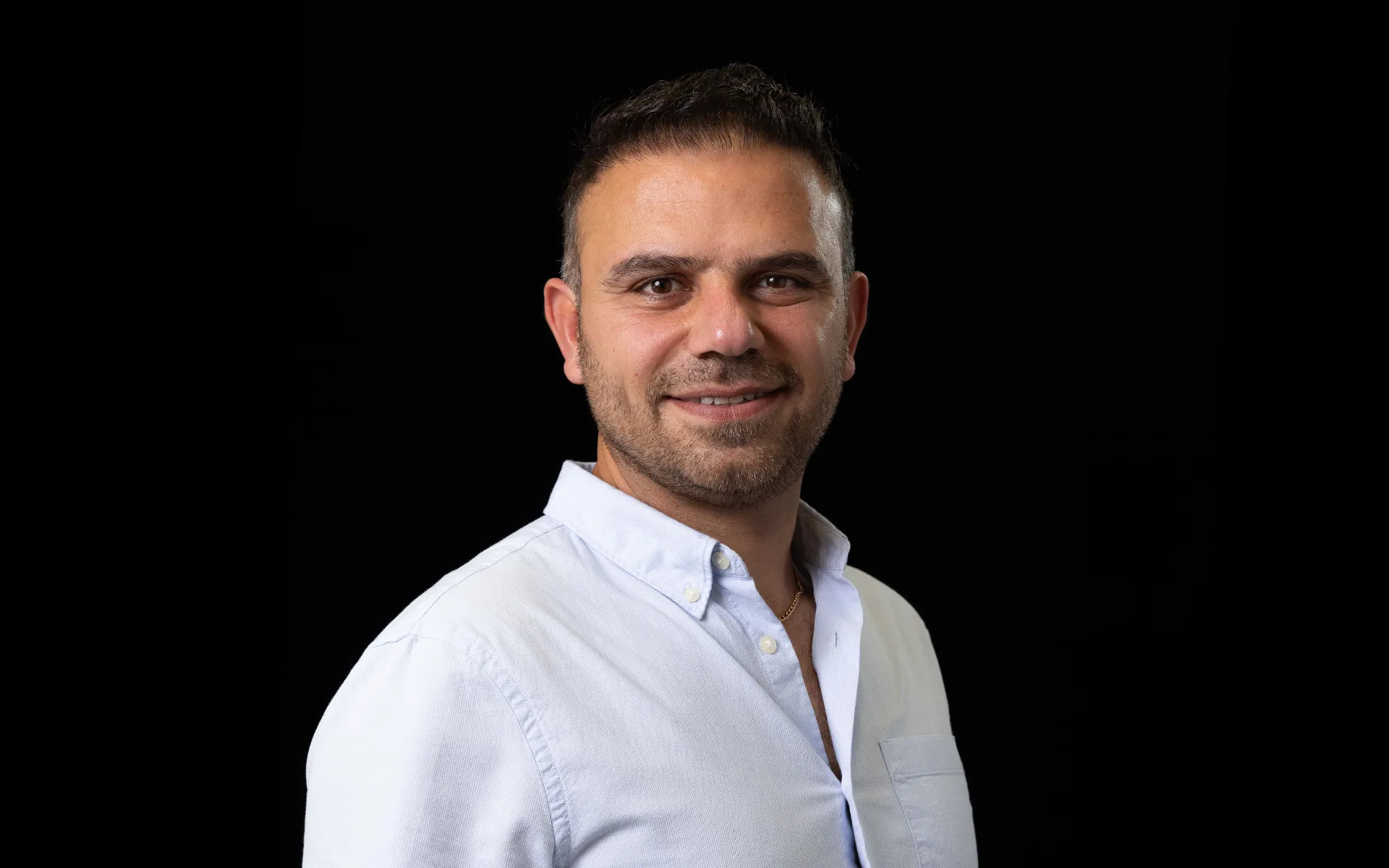 A portrait of Ali Sabzianpoor wearing a white shirt against a black background.