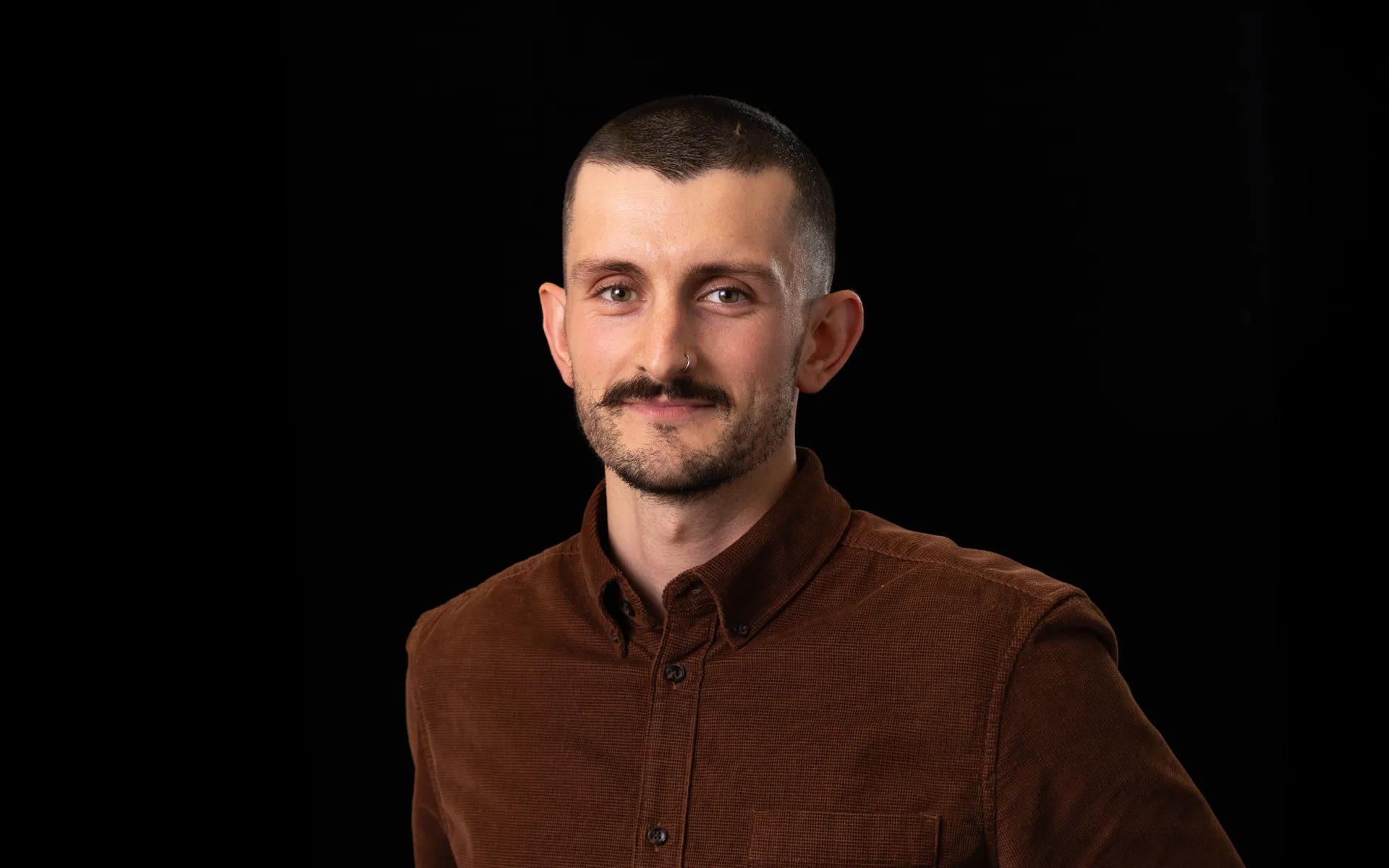 A portrait of Andrew Terry wearing a dark brown shirt against a black background.