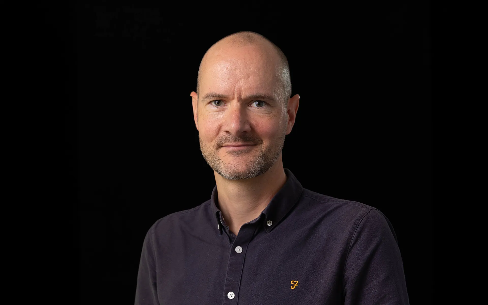 Portrait of Brian Moore wearing a dark shirt against a black background.