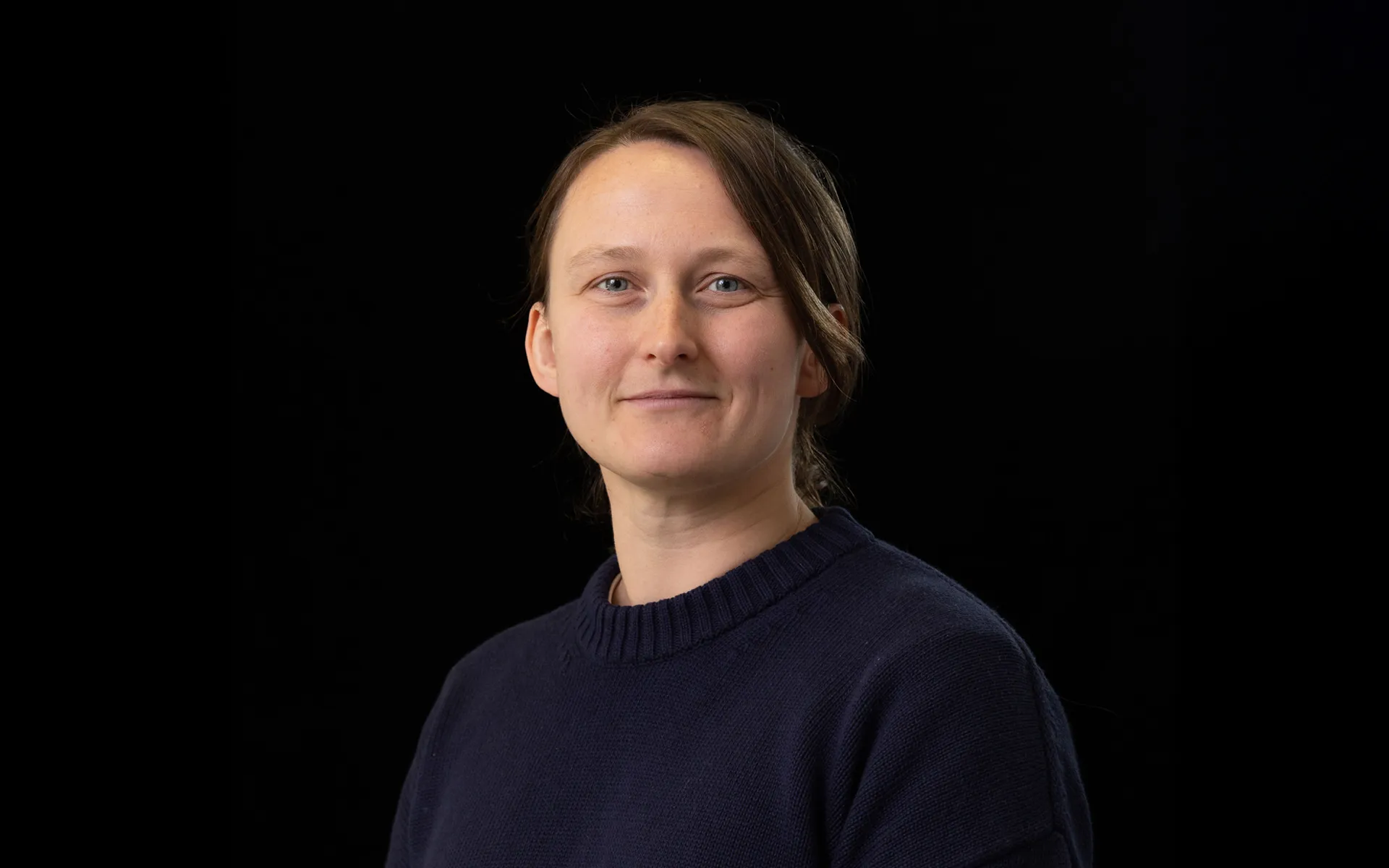 Portrait of Chloe Hurley wearing a navy jumper against a black background.