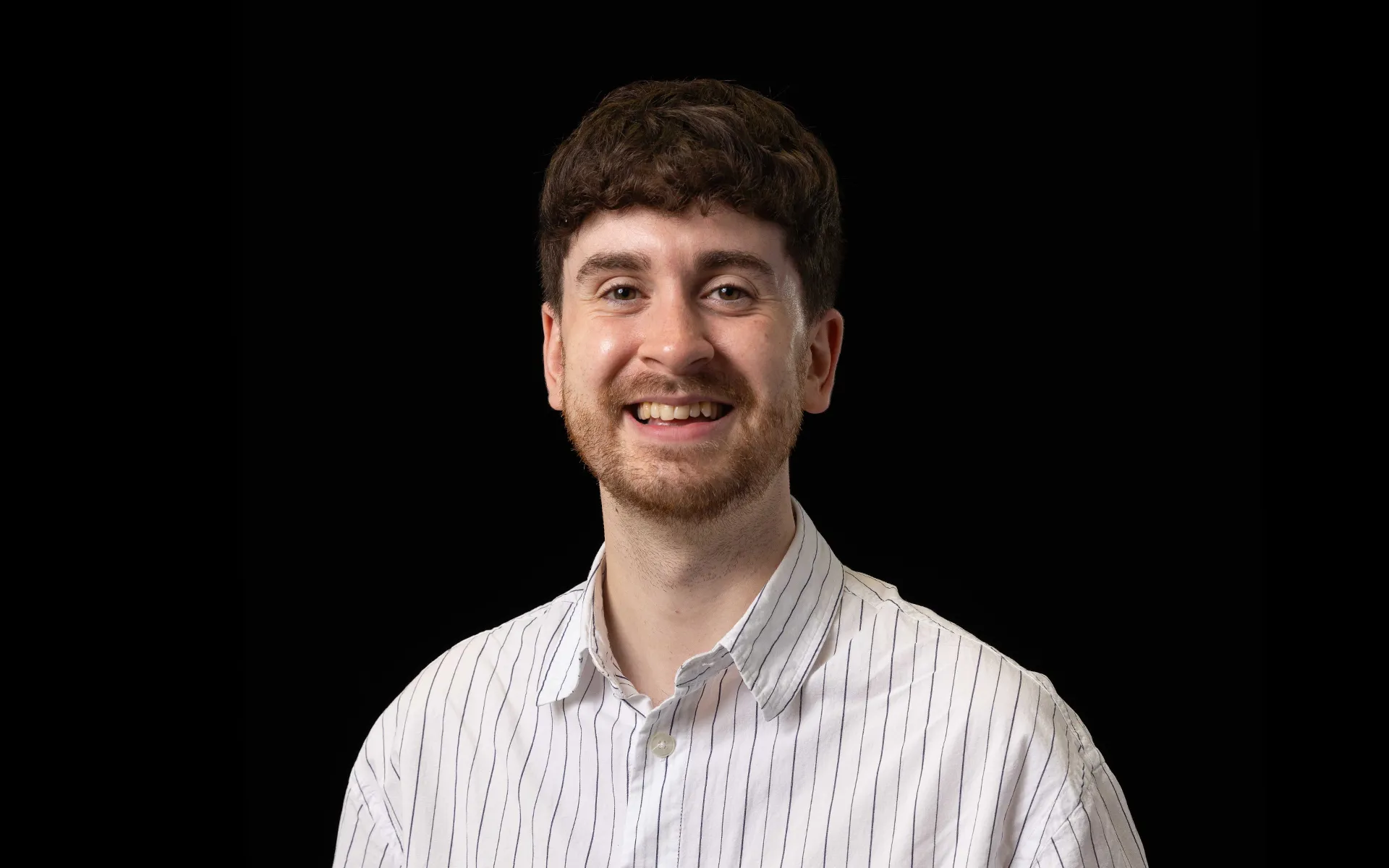 Portrait of Darren Callum wearing a white striped shirt against a black background.
