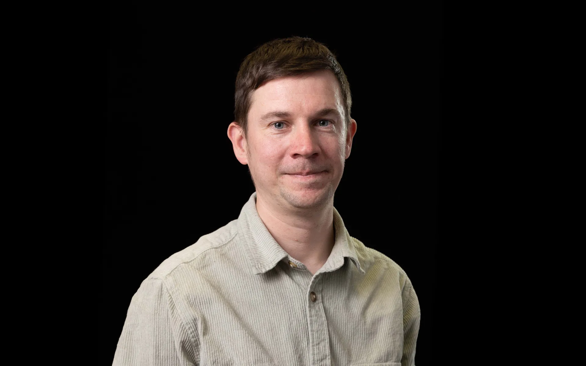 Portrait of David Leonard wearing a beige shirt against a black background.
