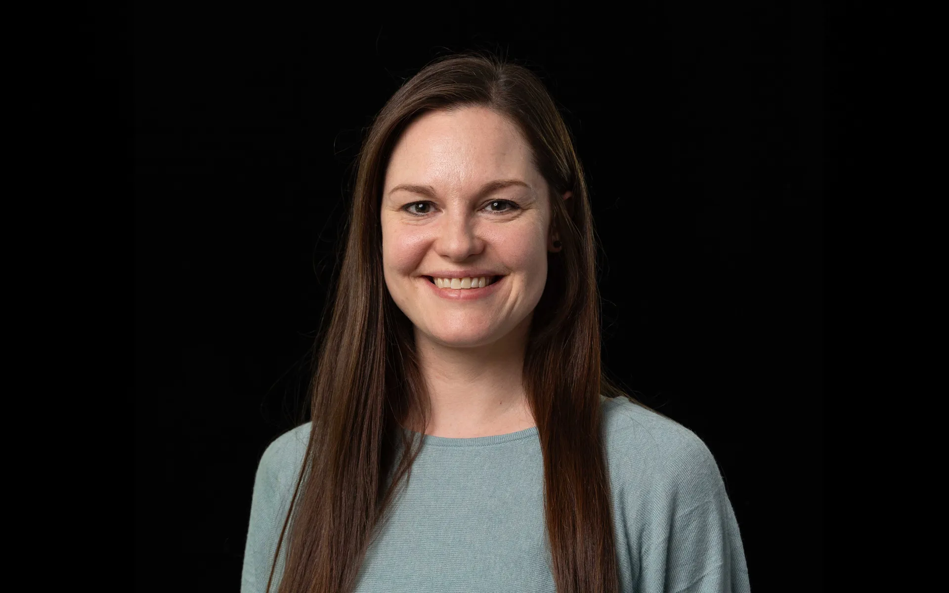Portrait of Dee Holden wearing a light blue top against a black background.