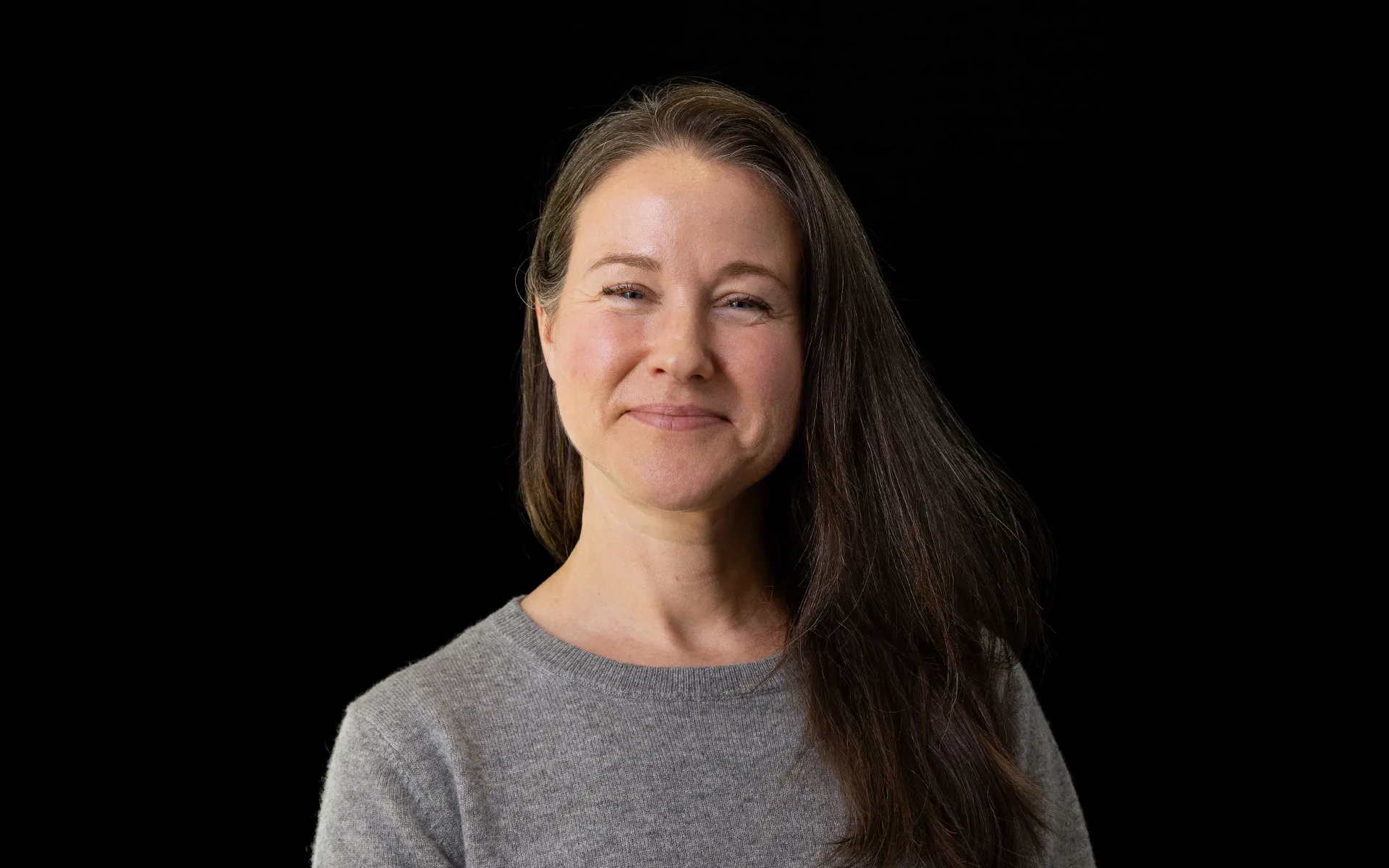 Portrait of Gill Pyatt wearing a grey jumper against a black background.
